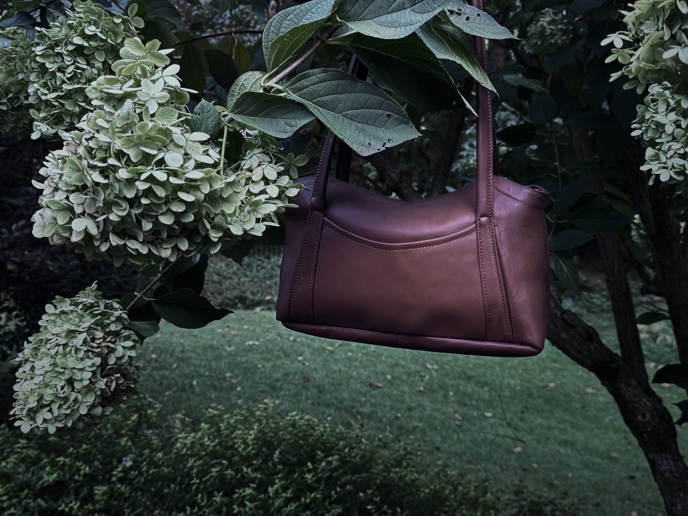 The Oxbo Shoulder hanging by its straps among hydrangeas at dusk